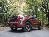 Red GMC truck equipped with Hercules Terra Trac AT X-Venture tires parked on a forest road, surrounded by tall trees with green and autumn-colored leaves.