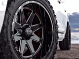 A close-up view of a TIS TT1 by Hercules that has a rugged tread design mounted on a sleek, multi-spoke black and chrome wheel. The vehicle is parked on a rocky surface with a scenic sky in the background, suggesting a rugged, outdoor environment.