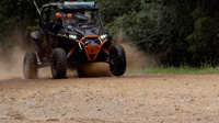 An orange and black UTV speeds across a dirt trail
