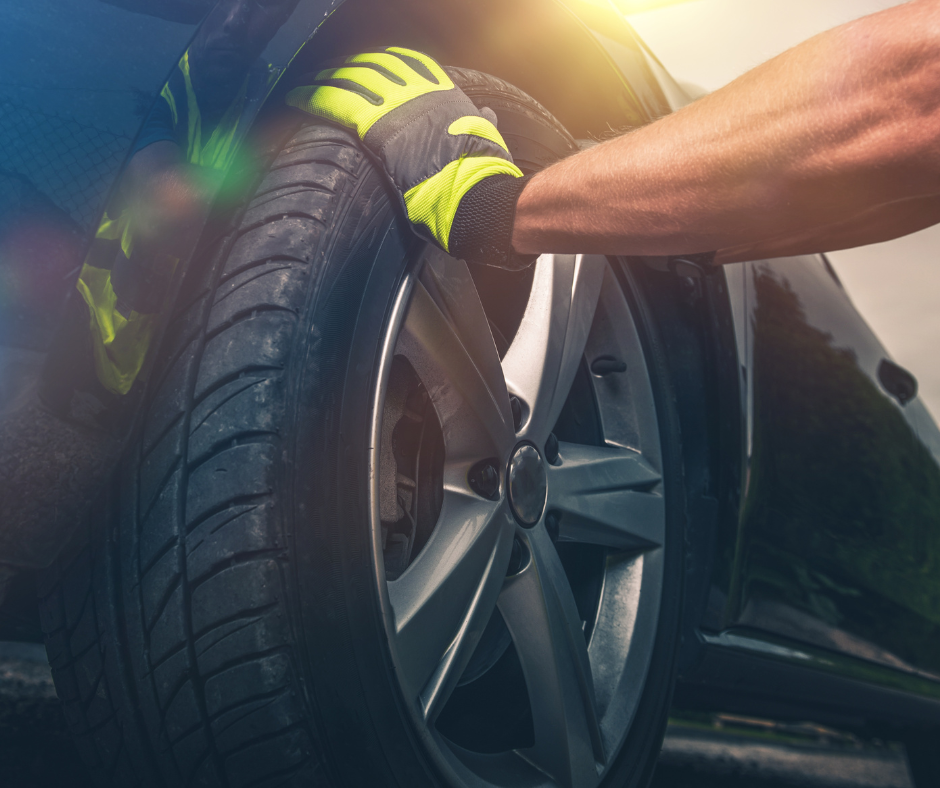 A close-up of a hand in a neon green maintenance glove pushing against a car tire.