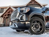 A close-up of a black pickup truck with Hercules Tires’ Avalanche TT winter tires parked in front of a snow-covered house, showcasing the rugged tread pattern designed for extreme winter conditions.