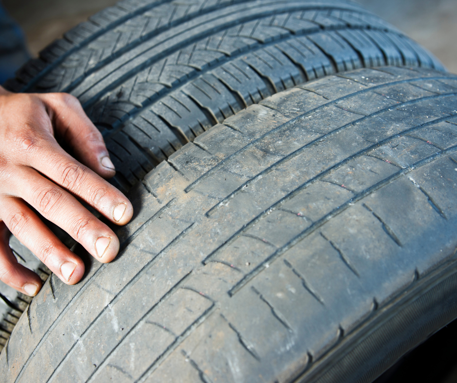 A hand over two tires that are side by side. One tire shows worn tire tread and the other shows a new tire with optimal tire tread depth.