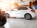 A white SUV parked in a garage with a tile floor. An ATV is peaking out from the right-hand corner and the garage door is open showing a sunny day.