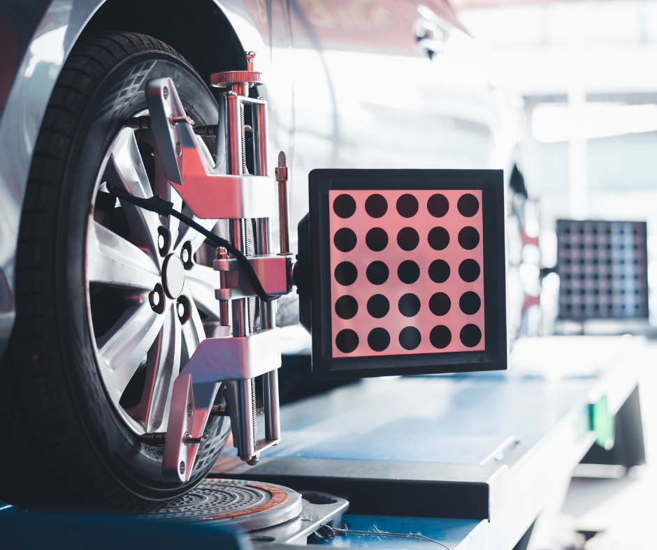 A car undergoing wheel alignment services is positioned on an alignment platform in a garage, with a close-up view of the equipment attached to the front wheel.