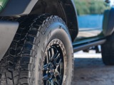 A close-up view of Hercules Terra Trac AT X-Venture tires on a green off-road vehicle, with a scenic background featuring a lake and trees.