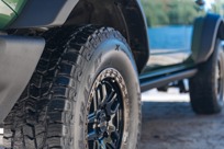 A close-up view of Hercules Terra Trac AT X-Venture tires on a green off-road vehicle, with a scenic background featuring a lake and trees.