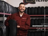 A smiling mechanic in a red jumpsuit holding a tire in a tire shop, with shelves of tires in the background. Text on the image reads: 'Supporting Independent Tire Dealers Since 1952.